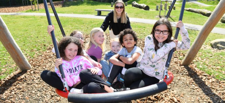 A Group Of Young People Are Pushed On A Swing By A Parent Aspect Ratio 785 360