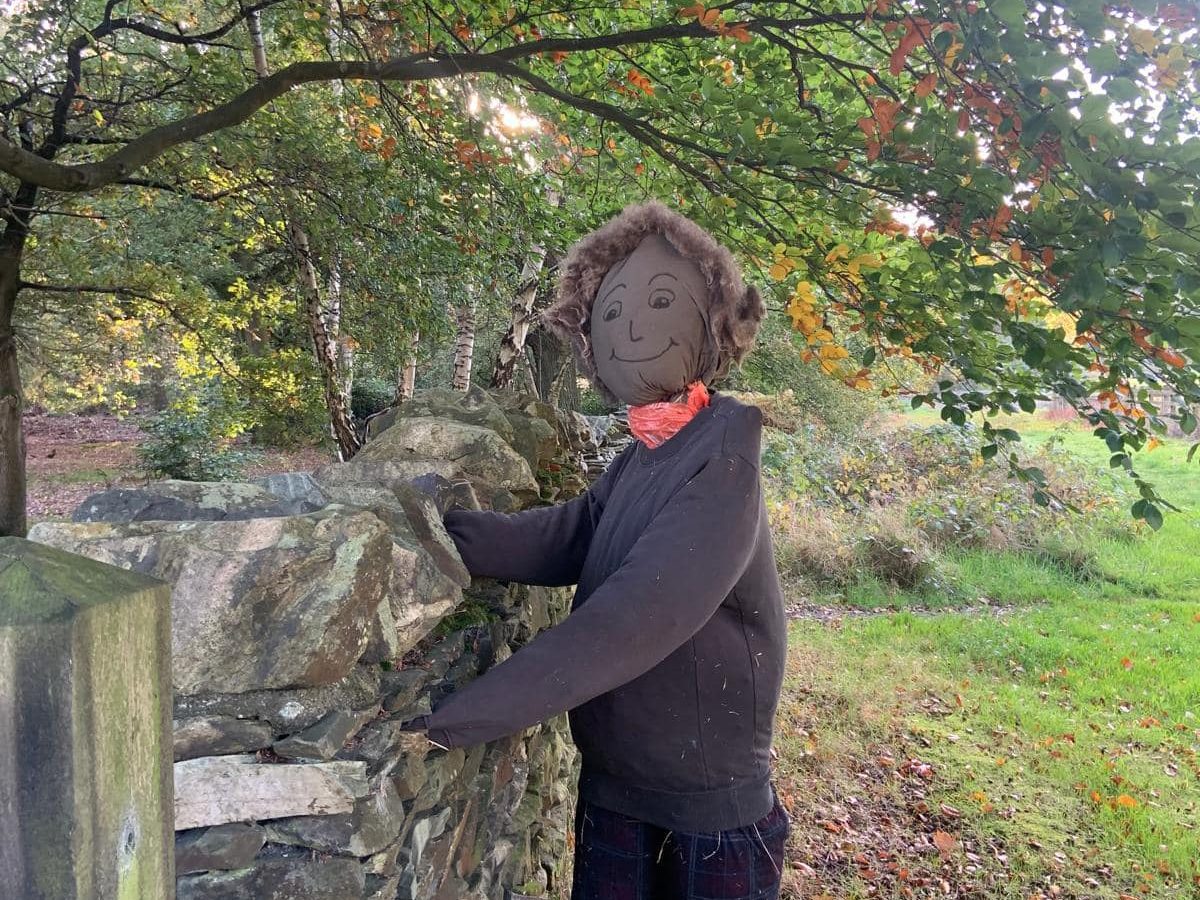 A scarecrow dressed up in black smiles at the camera. Located next to a fence in Beacon Hill