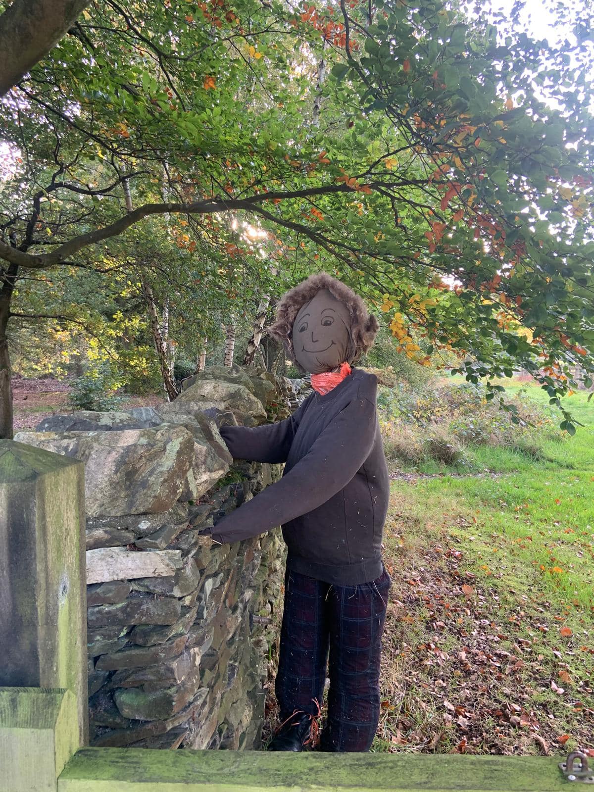 A scarecrow dressed up in black smiles at the camera. Located next to a fence in Beacon Hill